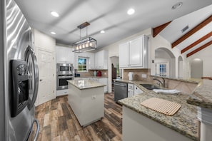 A modern kitchen with white cabinetry, granite countertops, stainless steel appliances, and a herringbone wood floor. - Private Hill Country Retreat 3-bedroom house with Resort Pool (Austin)