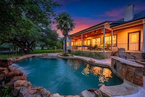 A pool with a stone border, a covered patio with chairs, and a house with a visible chimney. - Private Hill Country Retreat 3-bedroom house with Resort Pool (Austin)