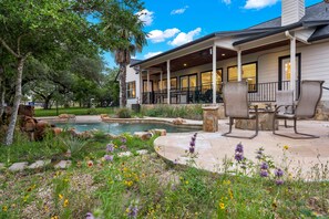 A covered outdoor patio with stone seating, a pool, and a landscaped garden. - Private Hill Country Retreat 3-bedroom house with Resort Pool (Austin)