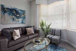 A living room with a brown sofa, striped armchair, and a glass coffee table. - The Clifton Townhouse, 5Bed with Hot Tub, King Bed (Scarborough)