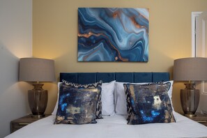 A bed with a blue headboard, two lamps, and a marble artwork on the wall. - The Clifton Townhouse, 5Bed with Hot Tub, King Bed (Scarborough)