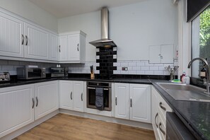 A modern kitchen with white cabinetry, a stainless steel range hood, and a black countertop. - The Clifton Townhouse, 5Bed with Hot Tub, King Bed (Scarborough)
