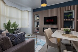 A modern living room with a sofa, coffee table, and a TV mounted on a wall with a Netflix sign. - The Clifton Townhouse, 5Bed with Hot Tub, King Bed (Scarborough)