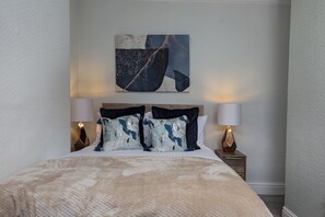 Een slaapkamer met een bed, twee bedlampen, een nachtkastje en een wanddecoratie in abstractie.