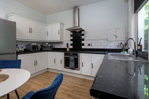 A modern kitchen with white cabinets, a black countertop, and a large window. - The Clifton Townhouse, 5Bed with Hot Tub, King Bed (Scarborough)