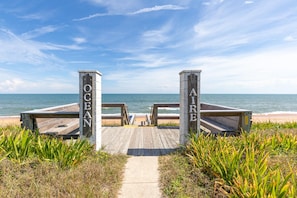 Ein Holzsteg führt zu einem Strand, an dem Wegweiser 'OCEAN AIR' stehen.