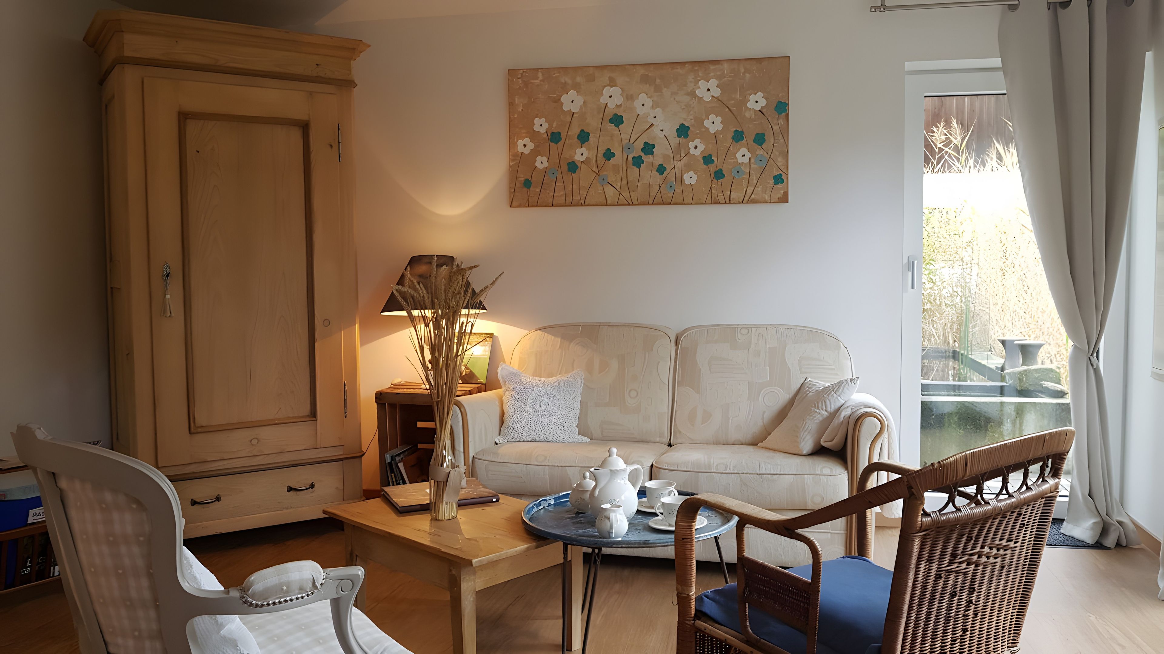 Ein Wohnzimmer mit Sofa, Schrank, Tisch mit Teeservice und einem Gemälde an der Wand.