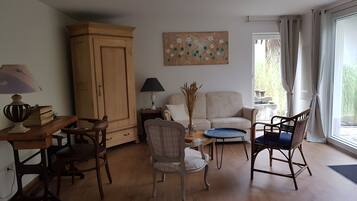 Una sala de estar con un mueble de madera, un sofá, una silla, una mesa con una lámpara y un cuadro en la pared.