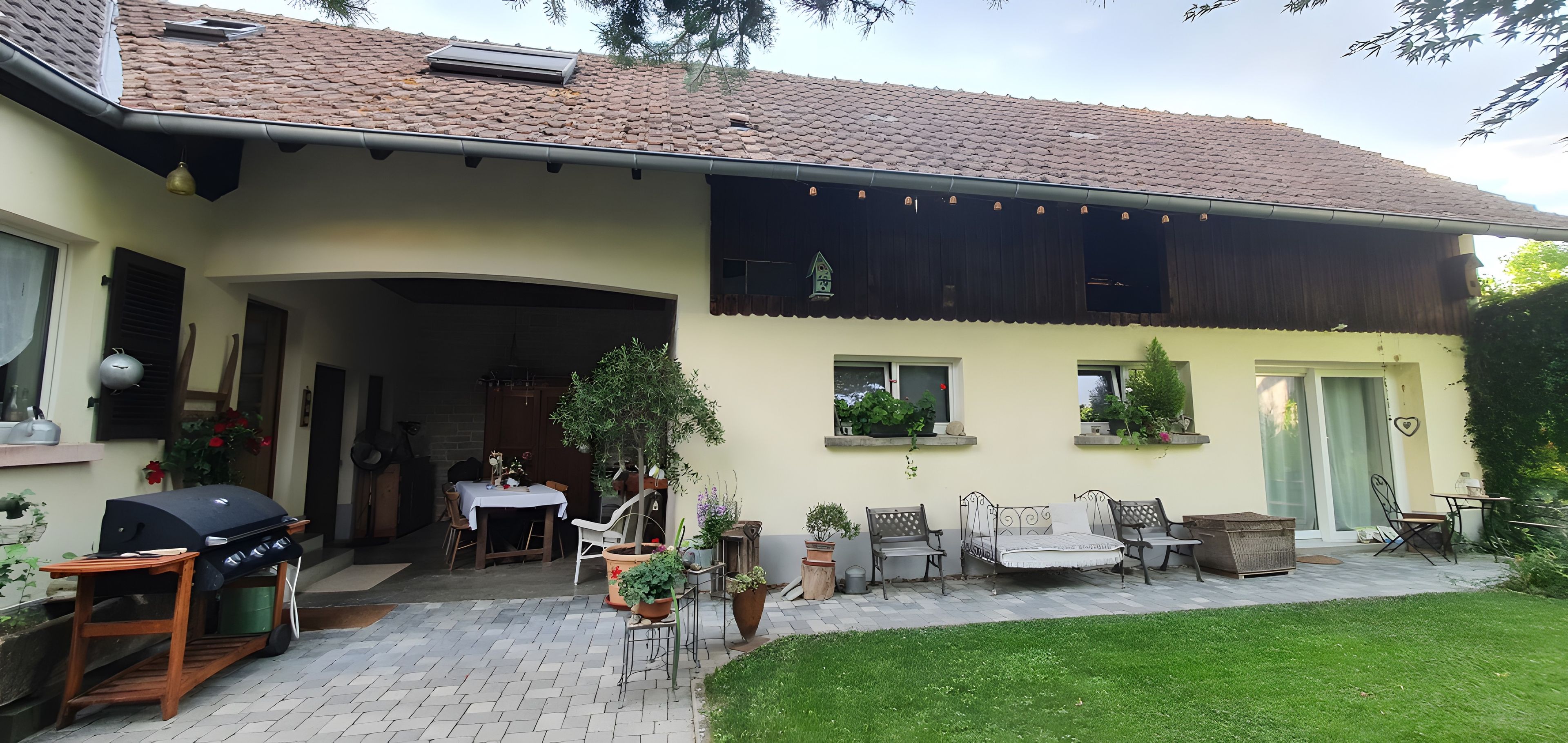 Ein Haus mit Terrasse, Gartenmöbeln und Blumentöpfen.