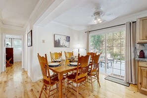A dining area with a wooden table set for four, surrounded by chairs, with a view of the outdoors through a glass door. - Mountain House 2 Miles to WCU  Hot Tub Fire Pit & BBQ Fishing and Climbing Nearby (Cullowhee)