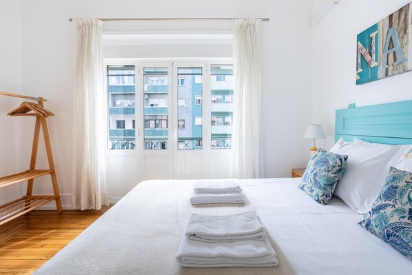 A hotel room with a bed, a wooden hanger rack, a window with a view of a building, and a blue headboard. - Casa da Avenida III Lisboa (Lisbon)