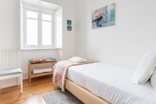 Un dormitorio con una cama, un banco, un ventanal y obras de arte en la pared.