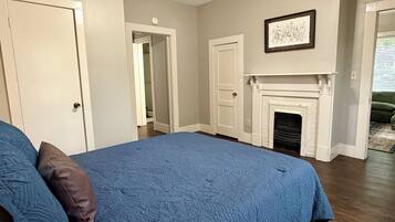 A bedroom with a large bed, a fireplace, and a door leading to another room.