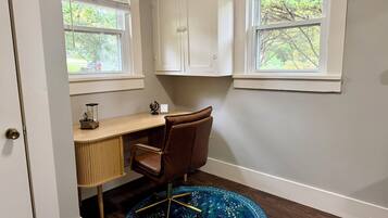 Un salón de estudio con un escritorio, una silla y dos ventanas con persianas.