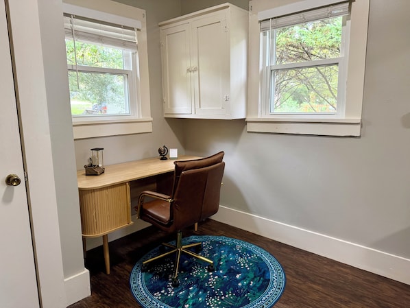 Un salón de estudio con un escritorio, una silla y dos ventanas con persianas.