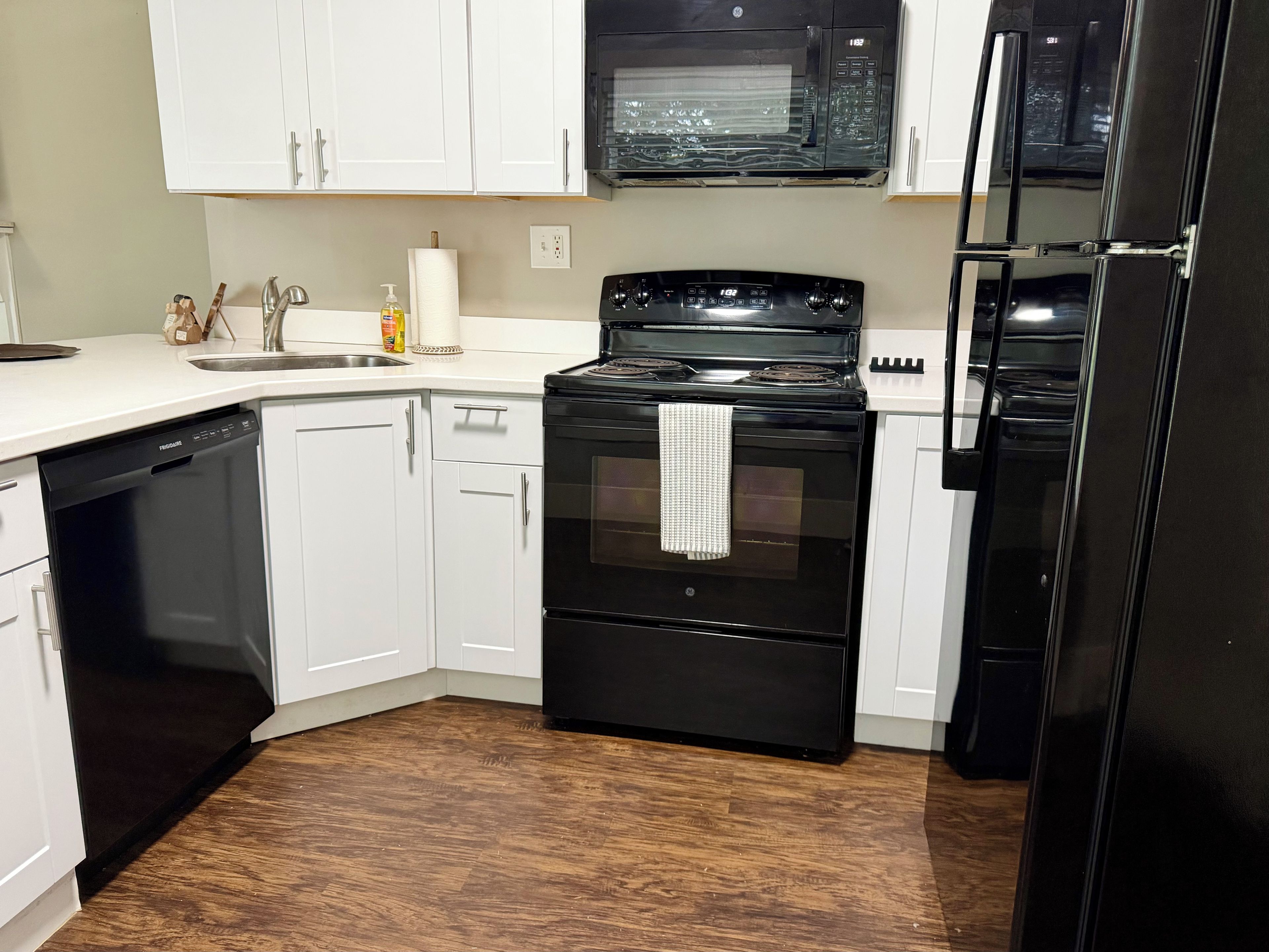 A kitchen with white cabinets, a black stove, a microwave, and a refrigerator.