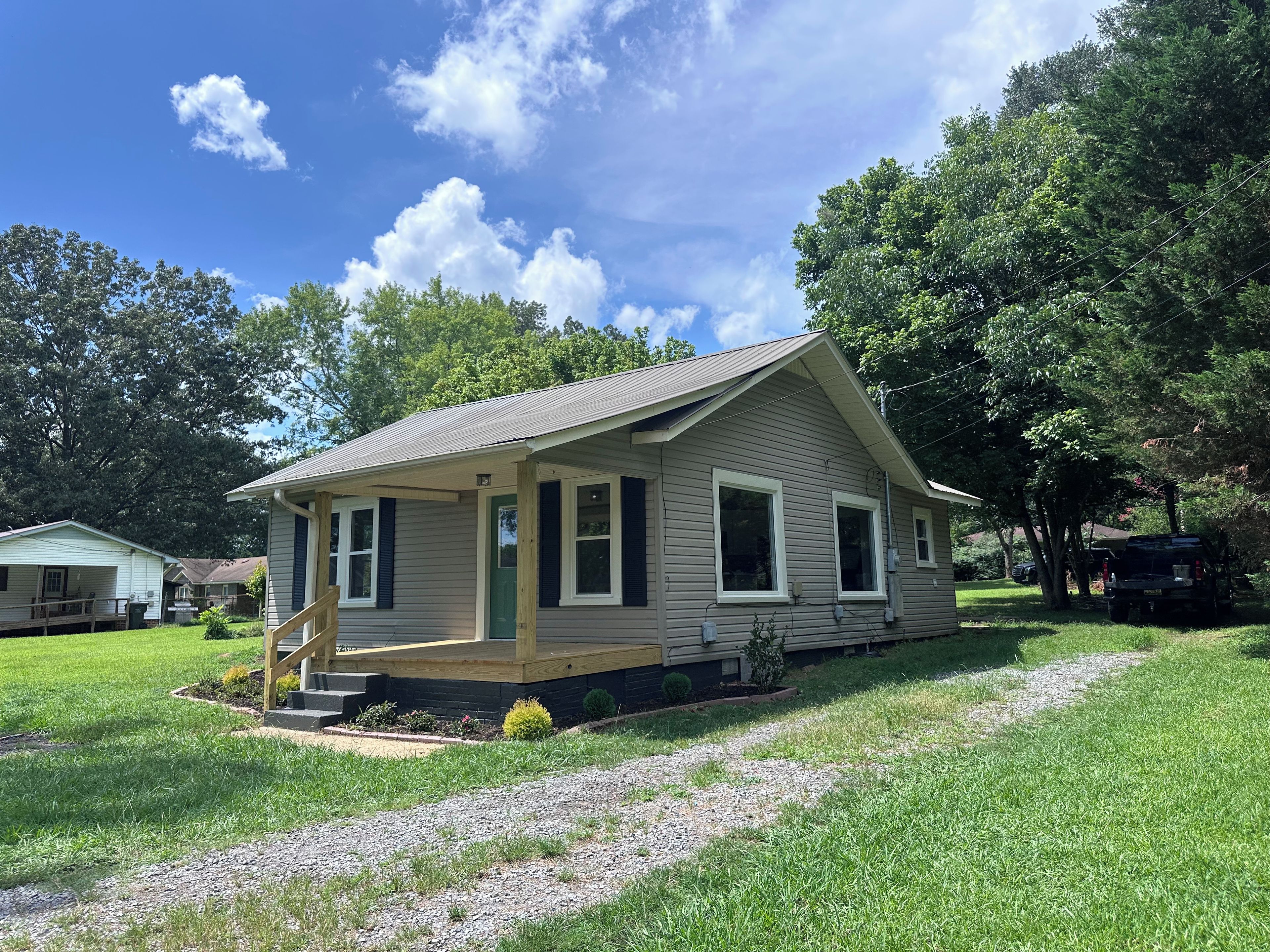 A single-story house with a front porch, a small deck, and a gravel driveway.