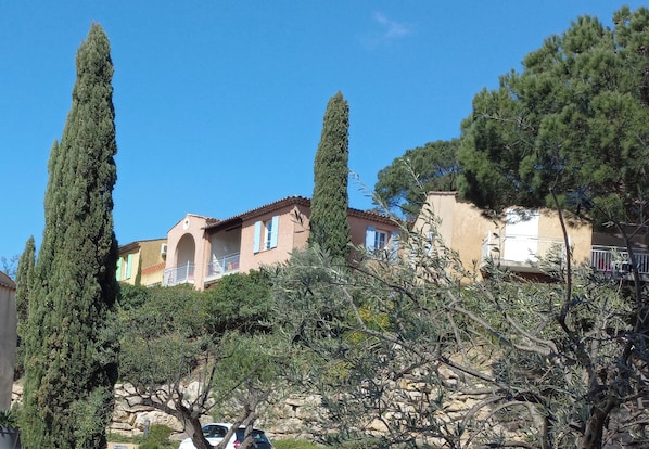 A residential building with a balcony, surrounded by tall cypress trees and other vegetation. - Les Bastides de Grimaud Apartment 407 in a quiet residence with a swimming pool. (Grimaud)