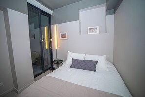 Un dormitorio con cama, mesita de noche con una planta y puerta corrediza de vidrio que da a otra habitación.