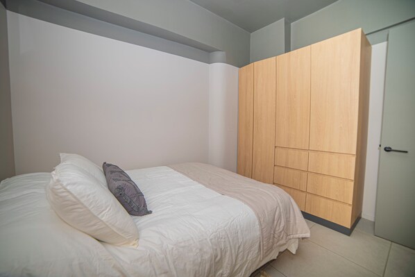 A bedroom with a bed, pillows, a wooden wardrobe, and a door. - 1-Bedroom Apartment + Terrace · Featured Design (H04) (Providencia)