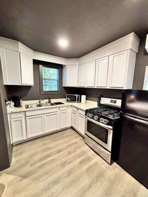 Cocina compacta con armarios blancos, microondas, estufa y refrigerador.