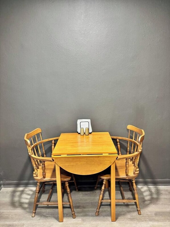 Una mesa de comedor con cuatro sillas de madera frente a una pared gris.