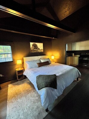 Un dormitorio con una cama grande, lámparas de noche, una ventana y una zona de cocina.