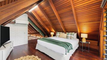 Ein Schlafzimmer mit schrägverdeckter Decke, einem Bett, Nachttischlampen, einem Fernseher und einer gewobenen Fußmatte.