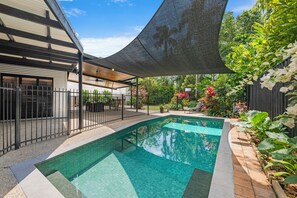 A swimming pool with a curved edge, surrounded by a fence and a shaded area.
