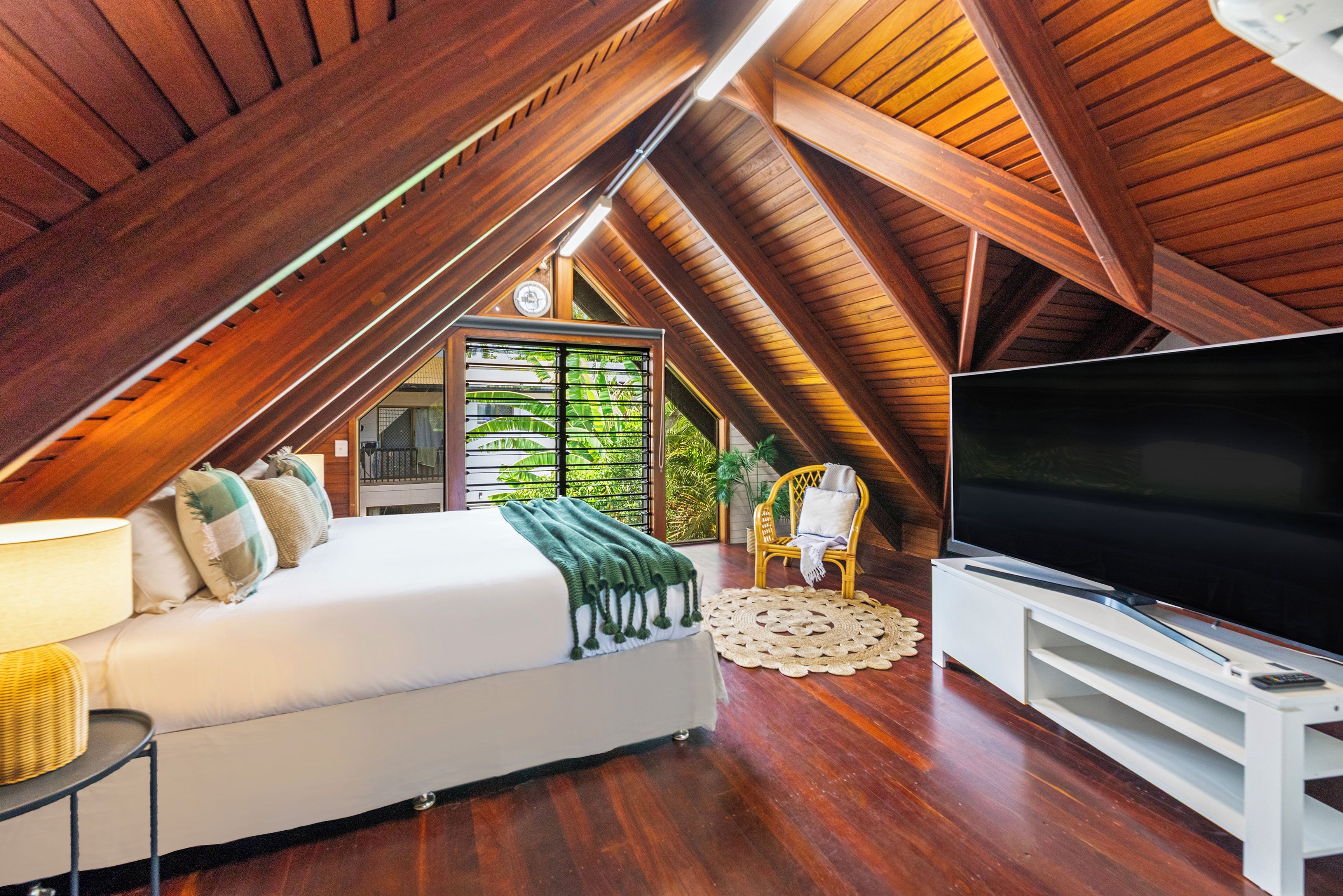 Une chambre aménagée dans les combles, avec un lit, une télévision et une vue sur la verdure environnante.