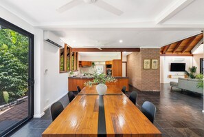 A modern kitchen with wooden cabinets, a central island, and a dining area with a long wooden table and chairs. - Serena Oasis Tropical Sanctuary with Private Pool (Nightcliff)