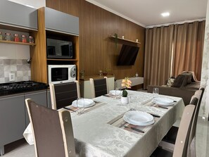 A modern kitchen with a dining area, a flat-screen TV mounted on the wall, and a sofa in the living room. - House Village A (Foz do Iguaçu)