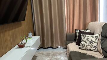 Una sala moderna con un televisor de pantalla plana montado en la pared, un sofá con cojines decorativos, una pequeña planta en maceta y una alfombra mullida.