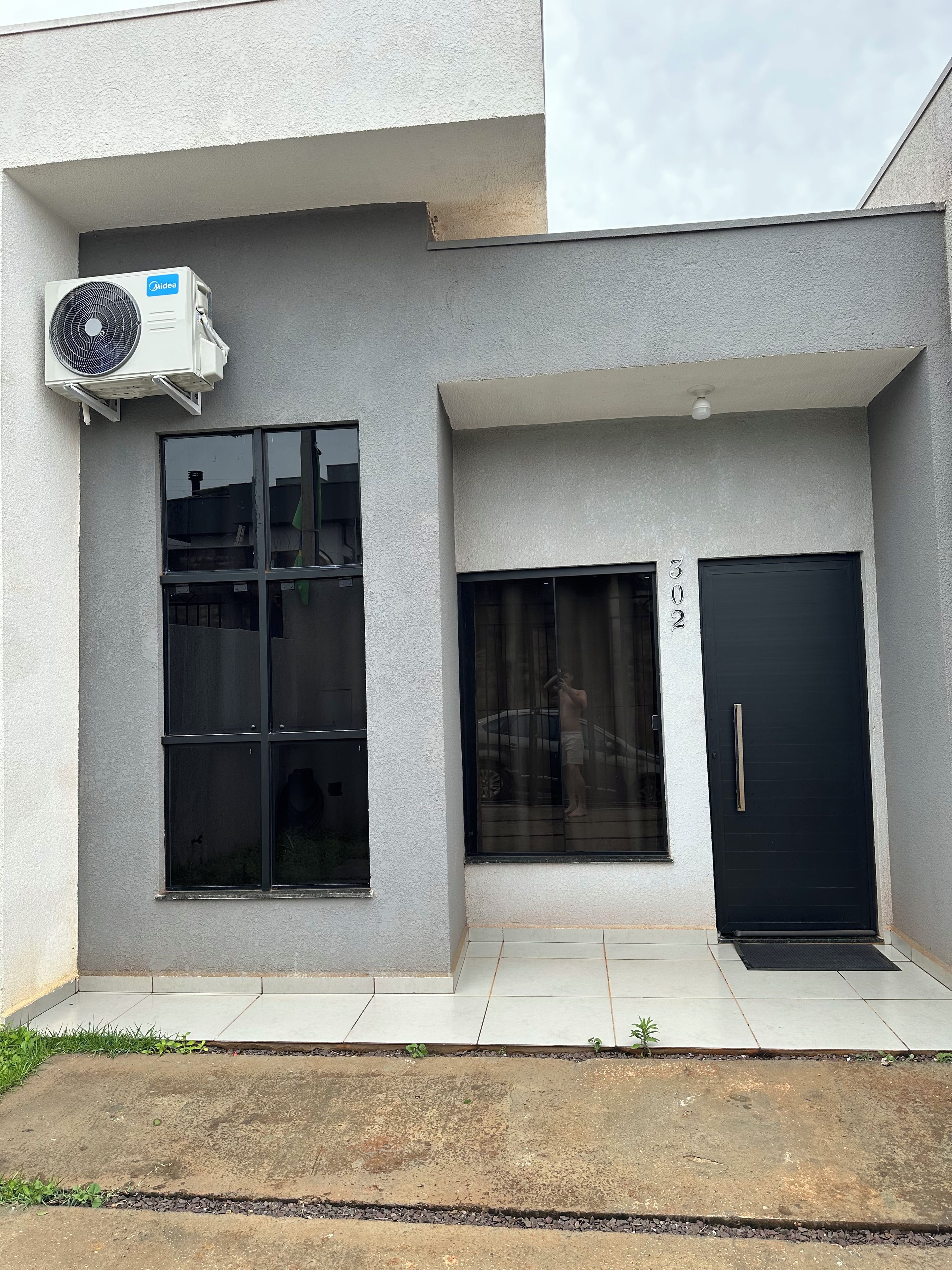 Un edificio con una unidad de aire acondicionado grande, una puerta negra con un número y una ventana que da a un coche.