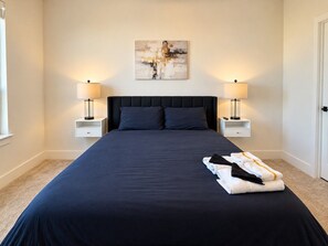 A hotel room with a large bed, two bedside tables with lamps, a painting on the wall, and a folded towel on the bed. - The Downtown Social | 2BR City Escape (Birmingham)