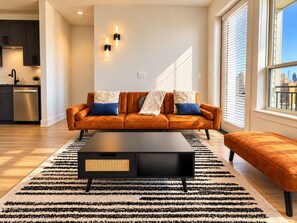 A modern living room with a sofa, ottoman, and coffee table. - The Downtown Social | 2BR City Escape (Birmingham)