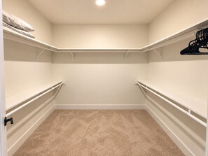 A closet with white shelving, a beige carpet, and a ceiling light. - The Downtown Social | 2BR City Escape (Birmingham)