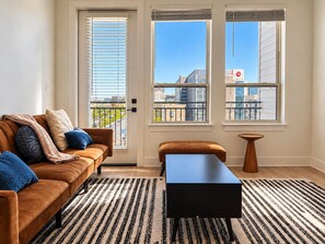 Ett modernt vardagsrum med en soffa, ett soffbord och utsikt över staden genom stora fönster.