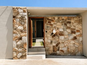 Entrada con muro de piedra, puerta de madera y escalones que llevan a un área cubierta.