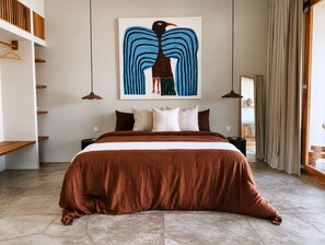 Ein Schlafzimmer mit einem großen Bett, einem Gemälde darüber und Blick ins Freie durch ein Fenster.