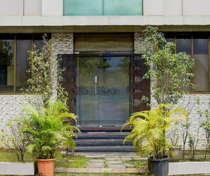 A building entrance with a dark wooden door, stone wall, and potted plants. - Deluxe Hotel Shivneri (Mumbai)