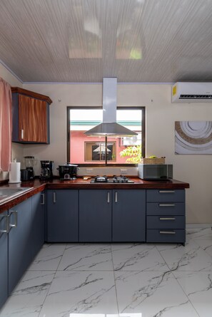 A modern kitchen with dark cabinets, a marble floor, and a window with a view. - Sun & Sea Twins Casa Sol (Savegre)