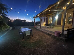 Un patio al aire libre con una mesa y sillas, luces colgantes y un área de estar techada.