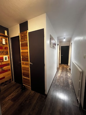 Un pasillo con piso de madera, una puerta negra y un radiador blanco.