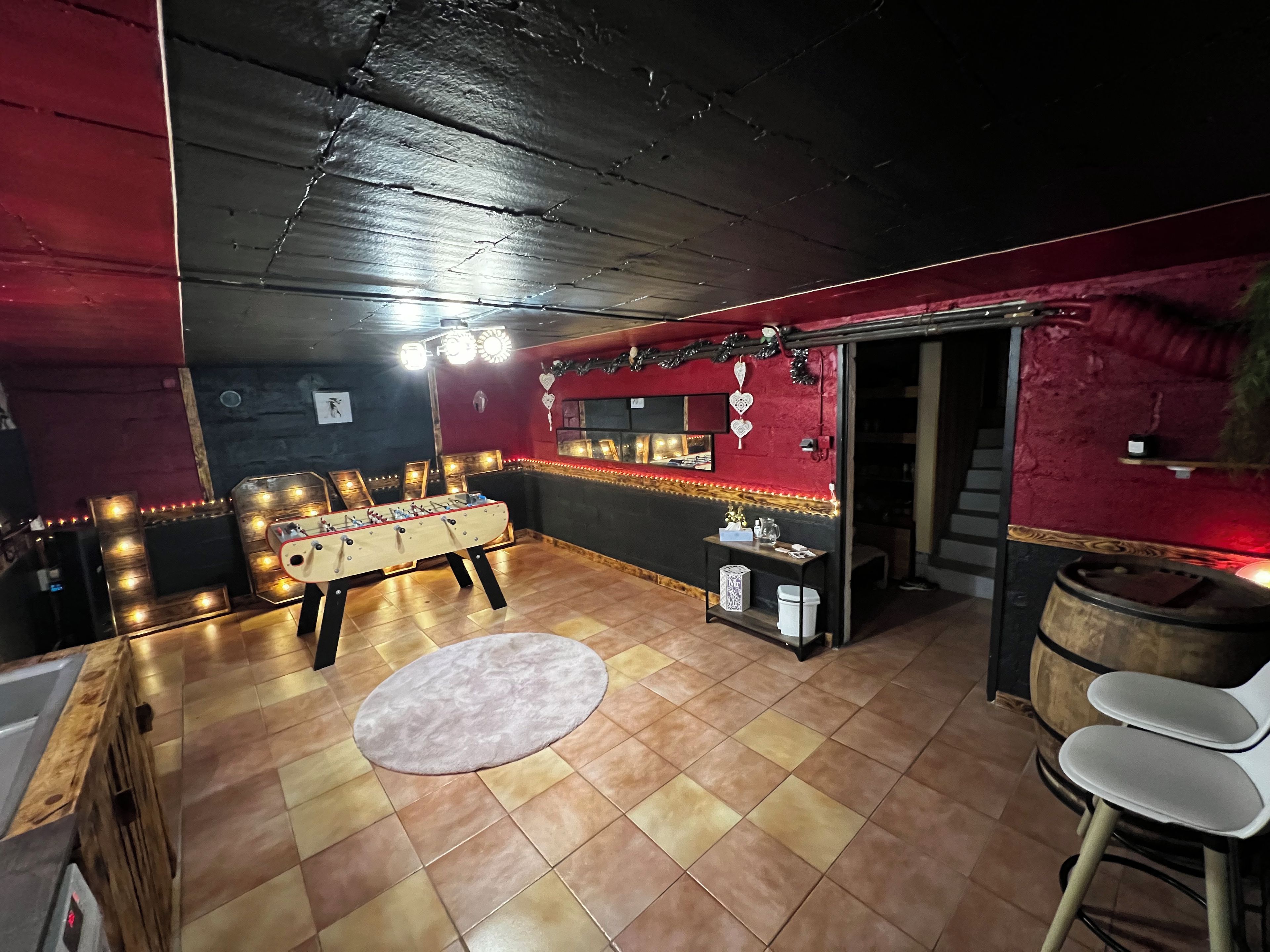 Una habitación con mesa de fútbol, alfombra redonda y zona de bar con taburetes.