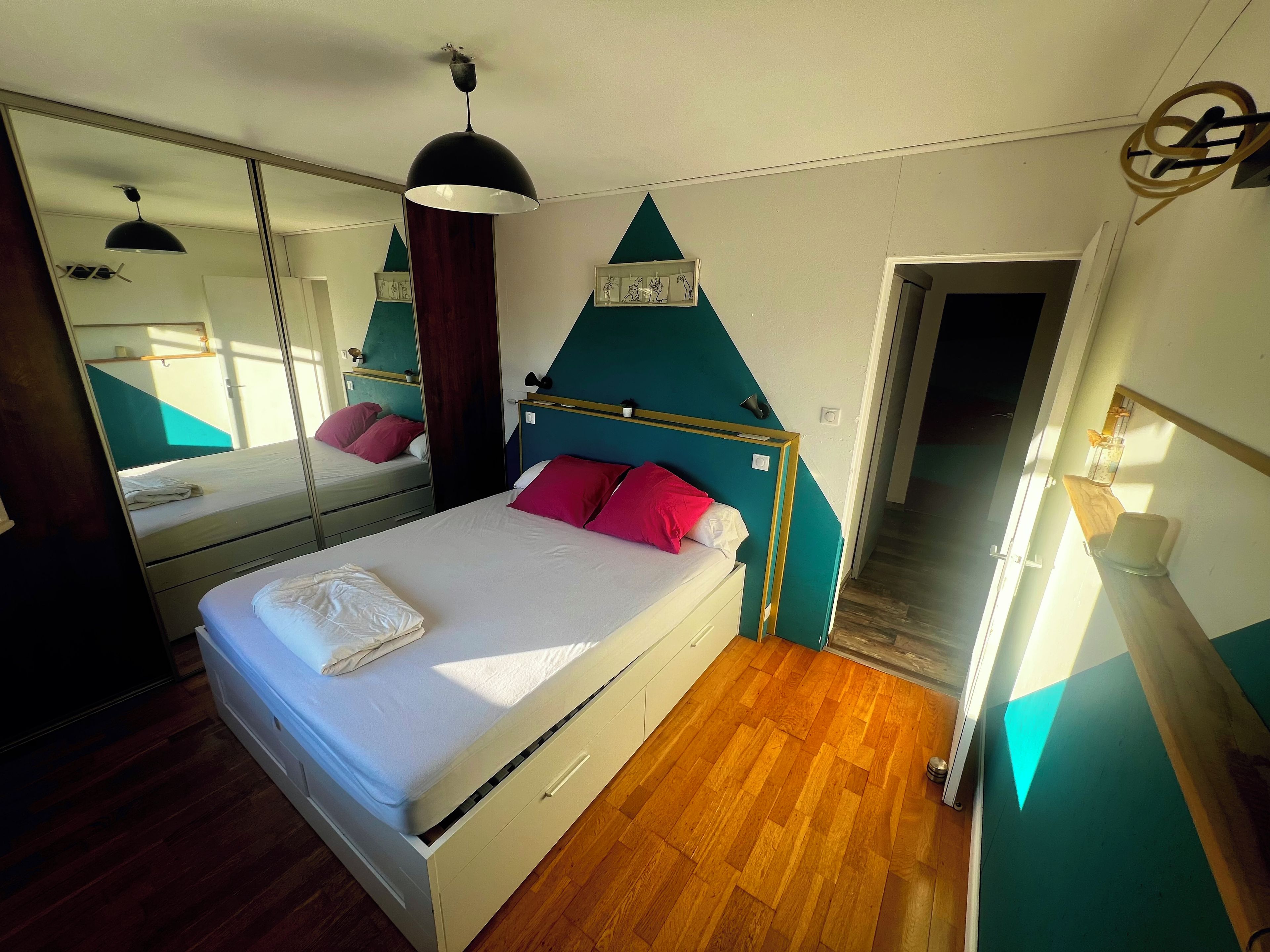 Un dormitorio con cama, cómoda, espejo y puerta que da a otra habitación.