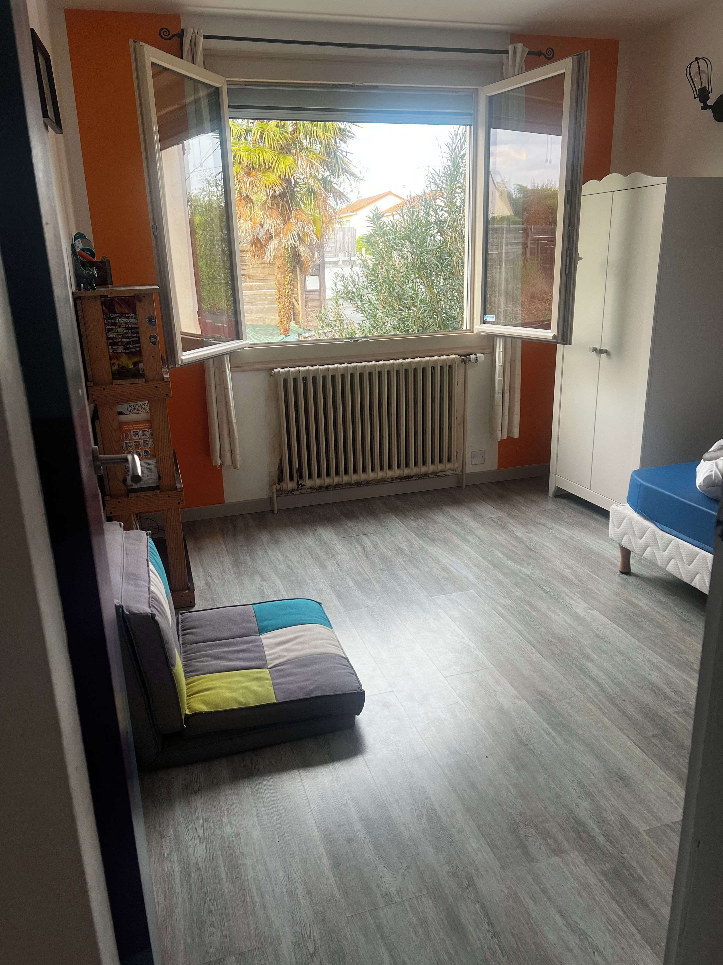 Un dormitorio con ventana, radiador, armario y una cama con colchón colorido.