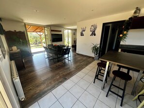 Un vaste espace de vie comprenant un coin repas avec table et chaises, un espace cuisine avec un bar, et une grande fenêtre laissant entrer la lumière naturelle.