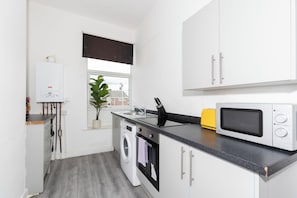 A compact kitchen with a washing machine, a microwave, and a sink. - Cape House- Cozy 1-bedroom studio, 4mins from Sunderland City Center (Sunderland)