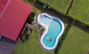 Una vista aerea di una piscina dalla forma particolare, circondata da un prato curato e un edificio con tetto rosso.